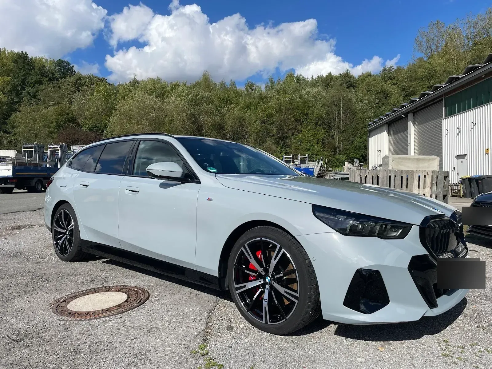 Hellgrauer BMW 5er Touring M-Paket steht bei Sonnenschein aufbereitet und glaenzend vor der Halle.