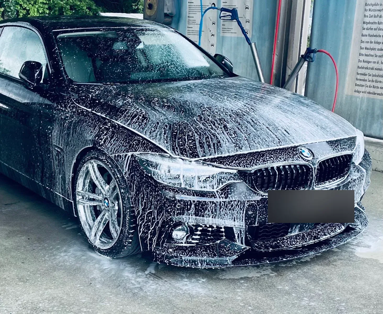 Schwarzer BMW 4er komplett mit Schneeschaum eingeschaeumt in einer Waschbox, Hochdrucklanzen im Hintergrund.