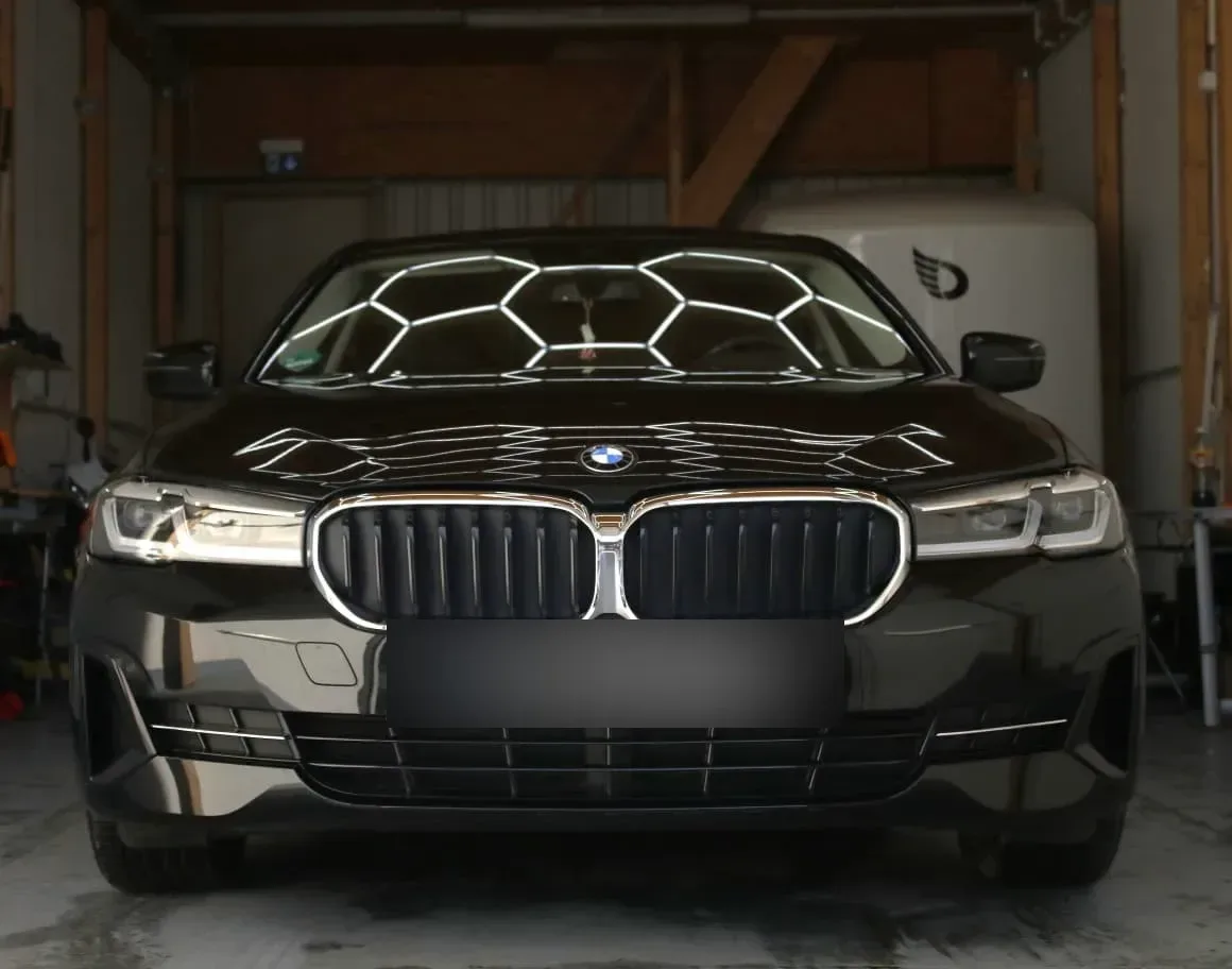 Frontale Aufnahme eines schwarzen BMW 5er in der Halle, Hexagon-Lichtreflexionen zeigen den spiegelglatten Lack nach der Politur.