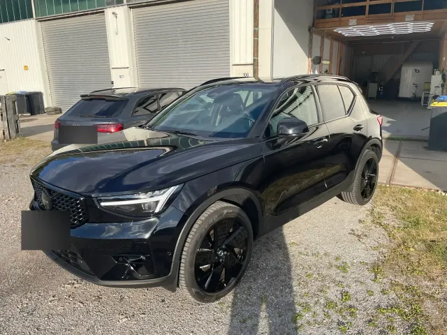 Schwarzer Volvo XC40 in Black-Edition mit spiegelndem Lack steht vor der Aufbereitungshalle mit beleuchteten Hexagon-Lampen im Hintergrund.