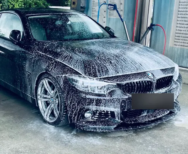 Schwarzer BMW 4er komplett mit Schneeschaum eingeschaeumt in einer Waschbox, Hochdrucklanzen im Hintergrund.
