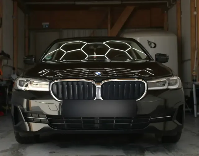 Frontale Aufnahme eines schwarzen BMW 5er in der Halle, Hexagon-Lichtreflexionen zeigen den spiegelglatten Lack nach der Politur.