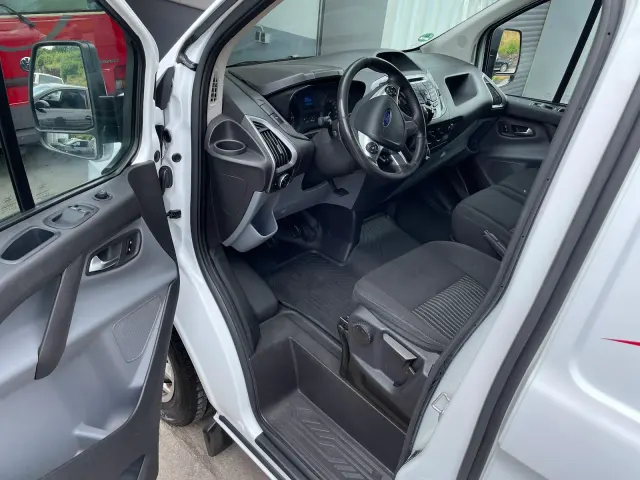 Offene Fahrertür eines weissen Ford Transit Custom mit sauberem Cockpit, gereinigten Stoffsitzen und ausgesaugtem Fussraum.