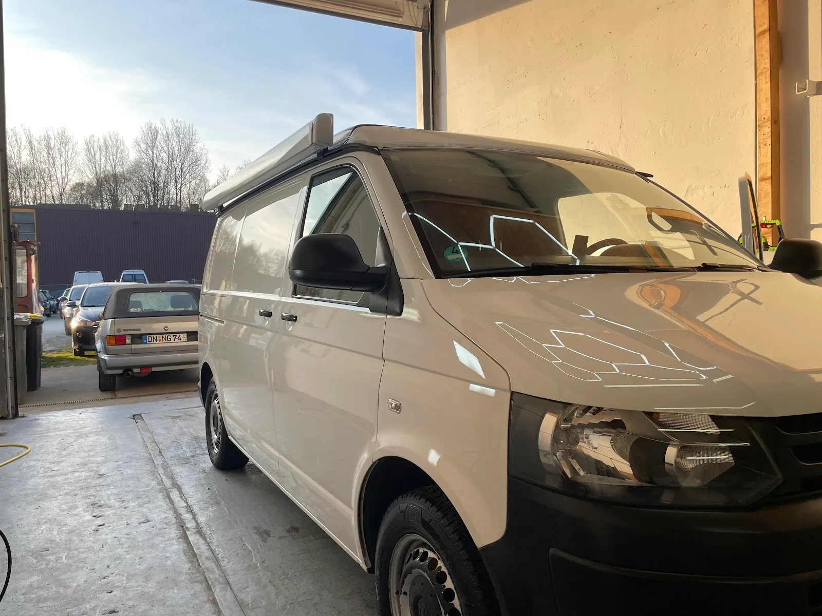 Weisser VW T5 Transporter steht im Hallentor, der Lack spiegelt die Fensterstreben nach der Aufbereitung scharf.